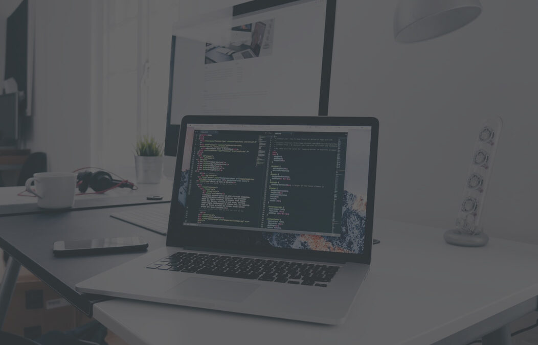 Laptop displaying source code beside a desktop monitor in a web development workspace