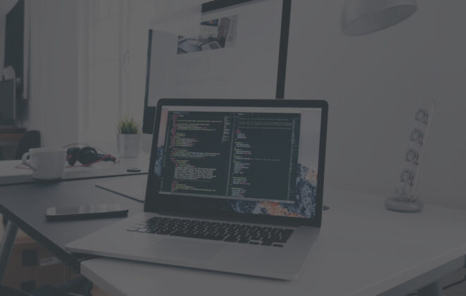 Laptop displaying source code beside a desktop monitor in a web development workspace